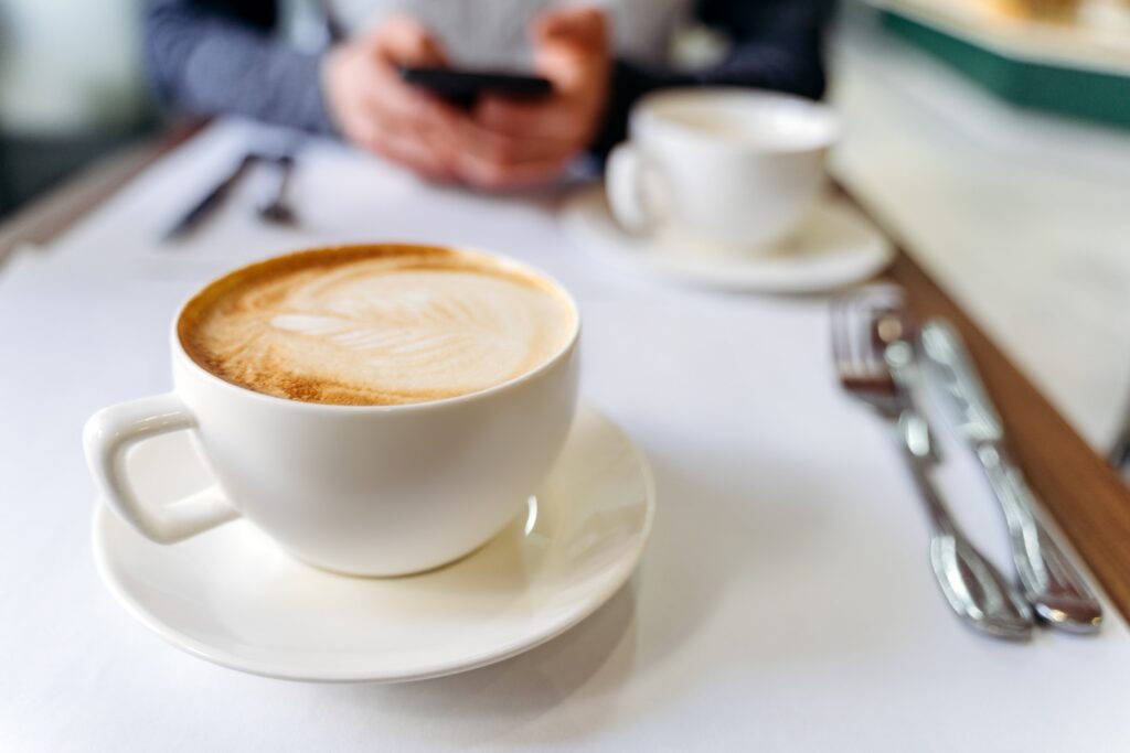 Cup with coffee on the table in a coffee shop. Man with phone on the background